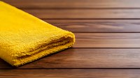 Yellow microfiber cleaning cloth folded on wooden surface with selective focus and copy space, showing texture and softness for household cleaning concept.