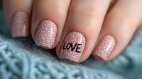 Romantic manicure in nude pink color with white polka dots pattern and black love lettering on ring finger nail. Close up of feminine nail art design.