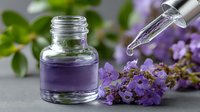 Lavender essential oil dropper bottle with fresh purple flowers and green leaves on gray background for aromatherapy and natural skincare.