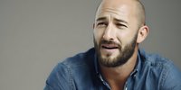 Bald man with beard expressing confusion or concern, wearing denim shirt against neutral gray background for advertising or emotional concept portrayal.