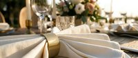 Elegant table setting with folded white napkins tied with gold ribbon, wine glasses, and floral centerpiece for fine dining events.