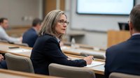 Professional mature businesswoman with glasses in corporate meeting room discussing strategy with colleagues during executive conference.