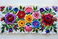 Traditional folk floral embroidery pattern with vibrant roses, daisies and leaves on white fabric featuring colorful red, pink, yellow and blue blooms in decorative style.