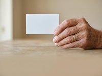Senior man with weathered hands holding blank white business card on wooden table, suitable for corporate identity mockups and professional branding presentations.