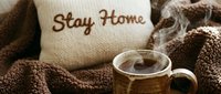 Cozy stay home scene with steaming hot coffee mug, knitted blanket, and embroidered pillow, evoking warmth, comfort, and relaxation.