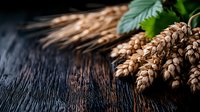 Fresh wheat ears with green leaves on dark rustic wooden background, dramatic lighting creates moody atmosphere for food photography and harvest concept.