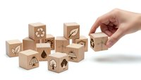 Hand placing wooden cube with eco symbols among sustainability blocks on white background for environmental awareness campaigns.
