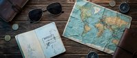 Vintage travel essentials arranged on wooden surface with world map, sketches, sunglasses, compass and leather accessories for adventure planning and exploration themes.