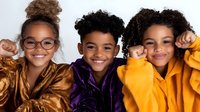 Three cheerful African American children wearing colorful cozy winter jackets smiling at camera against white background, studio portrait of siblings or friends.