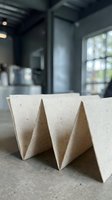 Corrugated cardboard packaging material with triangular wave design on concrete surface in modern industrial workspace with blurred background and natural window light.