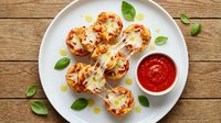 Mini pizza bites with melted cheese and fresh basil on white plate with marinara sauce, perfect appetizer for parties and gatherings on rustic wood.