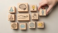 Hand arranging wooden blocks with mindfulness and mental health icons including meditation, brain, lightbulb, and communication symbols on neutral background.