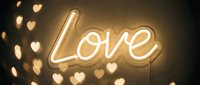 Glowing neon Love sign on a warm golden wall with soft bokeh heart lights, creating a romantic Valentine's Day or wedding atmosphere.