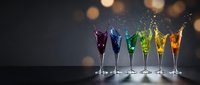 Colorful cocktails in champagne flutes with splashing liquid creating dynamic motion against bokeh background for celebration and party themes.
