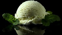 Creamy vanilla ice cream scoop with fresh mint leaves on reflective black surface, dramatic low-key lighting creates elegant mood for food photography and dessert menus.