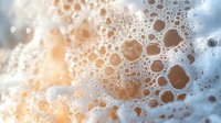 Soap bubbles and foam texture with warm golden light creating abstract background for cleaning products and bathroom concepts.
