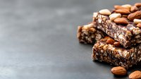 Homemade chocolate protein bars with almonds and nuts on dark background, healthy snack bars stacked with copy space for text on left side.