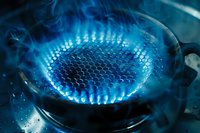 Blue gas flame burning on kitchen stove with honeycomb pattern, close up view showing heat energy and cooking surface in dark atmosphere.