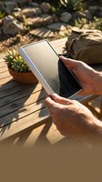 Hands holding tablet computer outdoors on wooden deck with succulent plants and natural sunlight shadows for digital lifestyle and technology use.