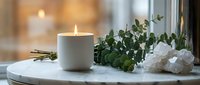 Peaceful spa setting with burning candle, eucalyptus branches and white towels on marble surface creating relaxing wellness atmosphere for meditation.