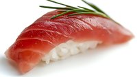 Fresh tuna nigiri sushi with rice and green chive garnish on white background, close-up view showing texture and detail of raw fish.