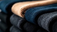 Neatly folded stack of cotton towels in various shades of blue, black and beige creating textural layers with selective focus on fabric weave pattern.