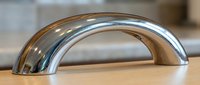 Modern chrome cabinet handle on wooden surface showcasing sleek curved design for contemporary kitchen and furniture hardware applications.