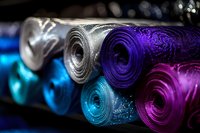 Colorful rolled yoga mats in vibrant purple, blue, pink and gray tones arranged on dark shelf with selective focus and bokeh effect, ready for fitness class.