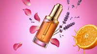 Luxury amber serum bottle with golden cap surrounded by floating rose petals, lavender sprigs and orange slice on pink gradient background for skincare advertising.
