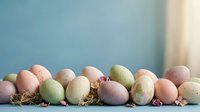 Colorful pastel Easter eggs in soft pink, green, and cream tones arranged with dried flowers on rustic surface for spring holiday celebration and decoration.