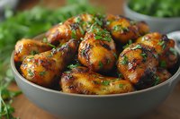 Grilled chicken drumsticks glazed with honey garlic sauce and fresh herbs in gray ceramic bowl, close up view of juicy meat with caramelized coating.