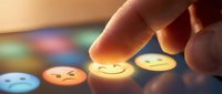 Finger pointing at glowing emoji button with happy face expression among colorful mood icons on dark surface, representing digital communication and emotional feedback selection.