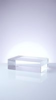 Clear acrylic rectangular block on a reflective white surface with soft purple gradient background, used as a modern product display podium.