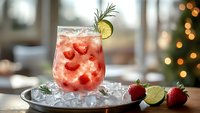 Fresh strawberry cocktail garnished with lime, rosemary and ice cubes on metal tray. Blurred bokeh lights and window background create cozy atmosphere.
