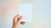 Hand holding blank white card against soft pastel gradient background, suitable for branding, business card mockups, and promotional material presentations.