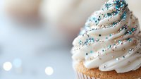 Vanilla cupcake with white frosting decorated with blue and silver sprinkles on blurred background for bakery menu and dessert advertising.