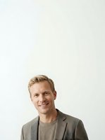 Blonde-haired male professional in his thirties with fair complexion wearing a gray blazer over a ribbed knit sweater, smiling at camera against neutral white background for corporate headshots and business portraits.