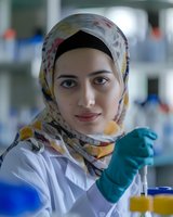 Middle Eastern female scientist in hijab working in laboratory setting with protective equipment and conducting research with test tubes and samples.