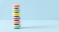 Colorful French macarons stacked in tower on pastel blue background. Sweet dessert cookies in pink, mint green, yellow and purple colors for bakery menu.