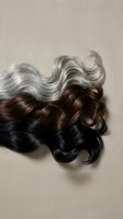 Wavy hair strands in gradient colors from black to brown to silver gray on neutral background showing natural aging process and hair color transition.
