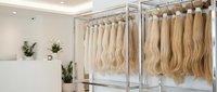 Professional hair extension salon display with blonde human hair pieces hanging on metal racks in modern beauty studio interior for styling services.