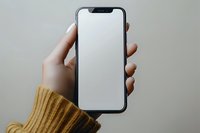 Female hands in yellow knit sweater holding modern smartphone with blank white screen against neutral background. Mockup for app or website design.