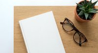 Blank white notebook with eyeglasses and succulent plant on wooden desk surface for office workspace mockup and business planning concepts.