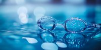 Swimming goggles with water drops on blue aquatic background with bokeh lights, reflecting pool surface creates dreamy atmosphere for sports and fitness concepts.