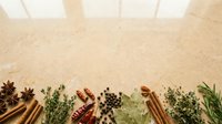 Overhead flat lay arrangement of dried herbs, spices and seasonings including cinnamon sticks, star anise, peppercorns and fresh green herbs on neutral beige background for culinary and cooking design projects.