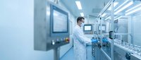 Male scientist in white lab coat working with advanced manufacturing equipment in sterile pharmaceutical cleanroom facility for medical research.