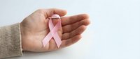 Female hands in beige sweater gently holding pink ribbon symbol for breast cancer awareness campaign and support on clean white background.