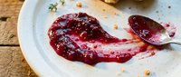 Homemade berry jam spread on white plate with wooden spoon, rustic table setting for cooking, baking, food preparation, and recipe content.