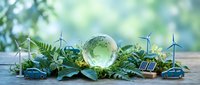 Crystal globe surrounded by green ferns and miniature wind turbines on wooden surface with soft natural lighting for environmental sustainability concepts.
