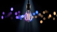 Vintage Edison bulb glowing with warm filament against dark background with colorful bokeh lights creating atmospheric lighting for creative projects.